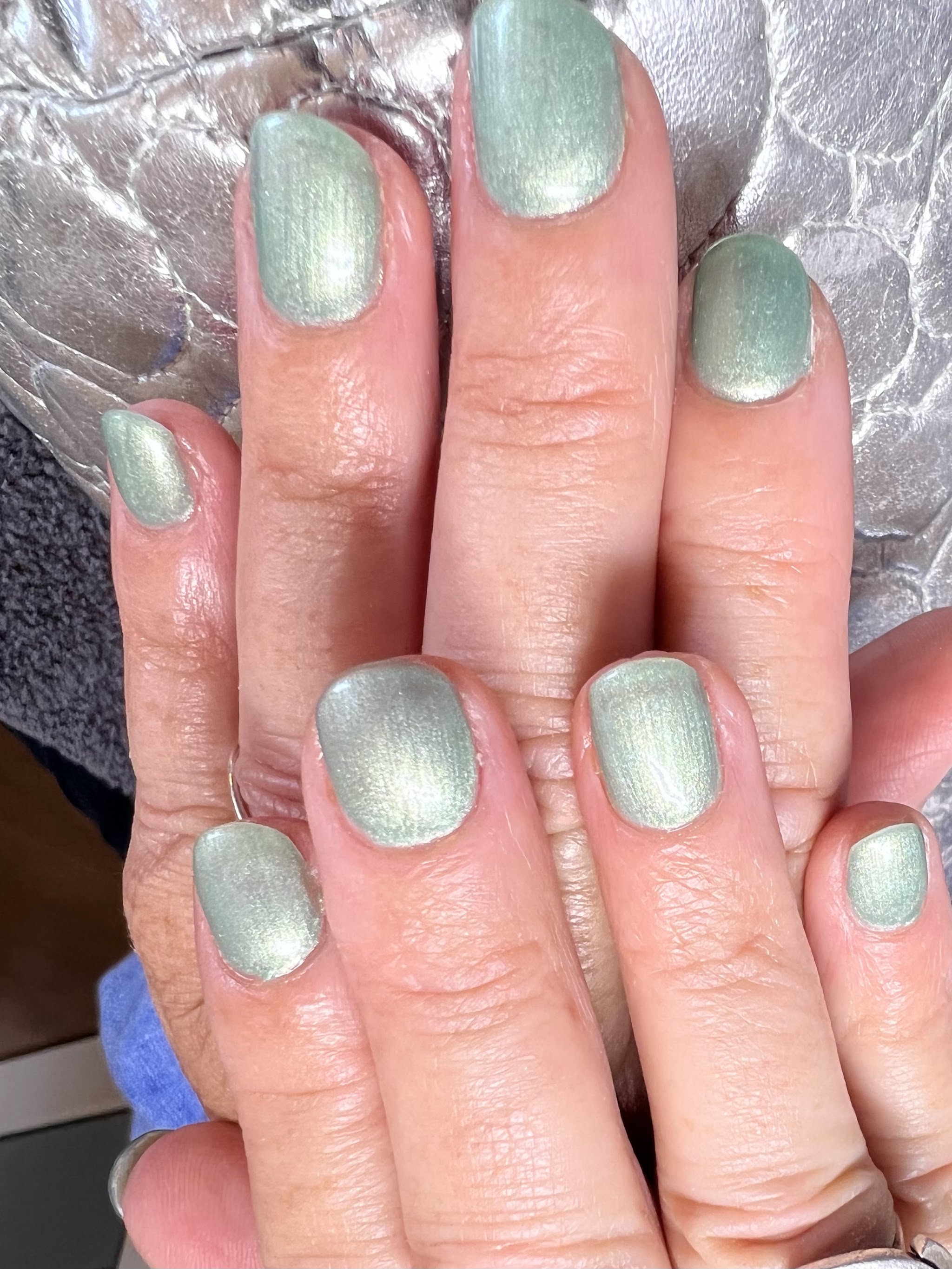 Korte nagels in een glanzende saliegroene chrome kleur